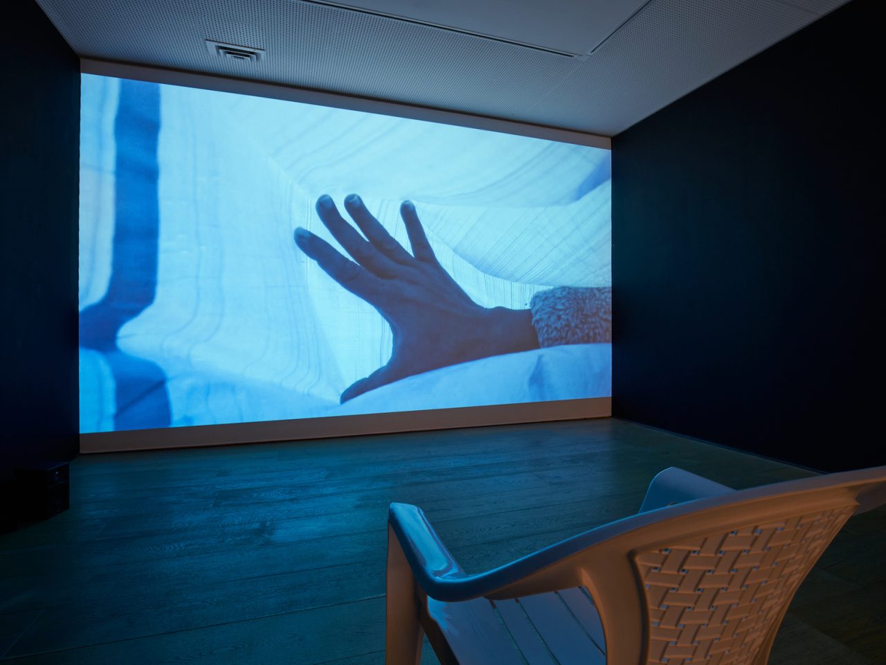 A film projection of someones hand beneath a a blue sheet.