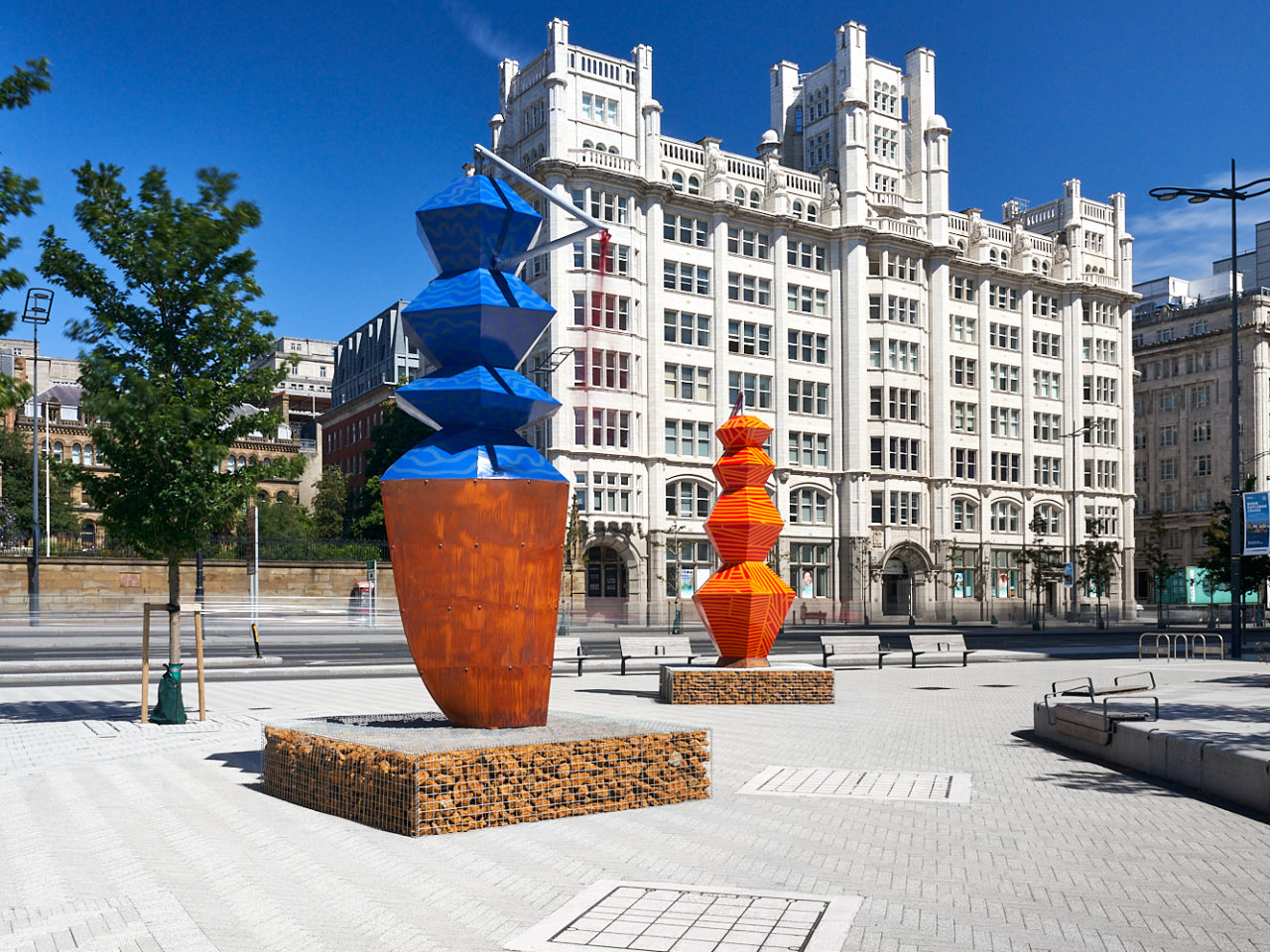 Two totems on Princes Dock, one geometrically painted red and yellow and one painted blue and the bottom half is covered in rust.