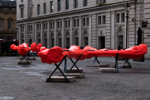A installation within Exchange Flags, there are multiple large bone shaped canoes, they are bright red and are sat on metal stands.