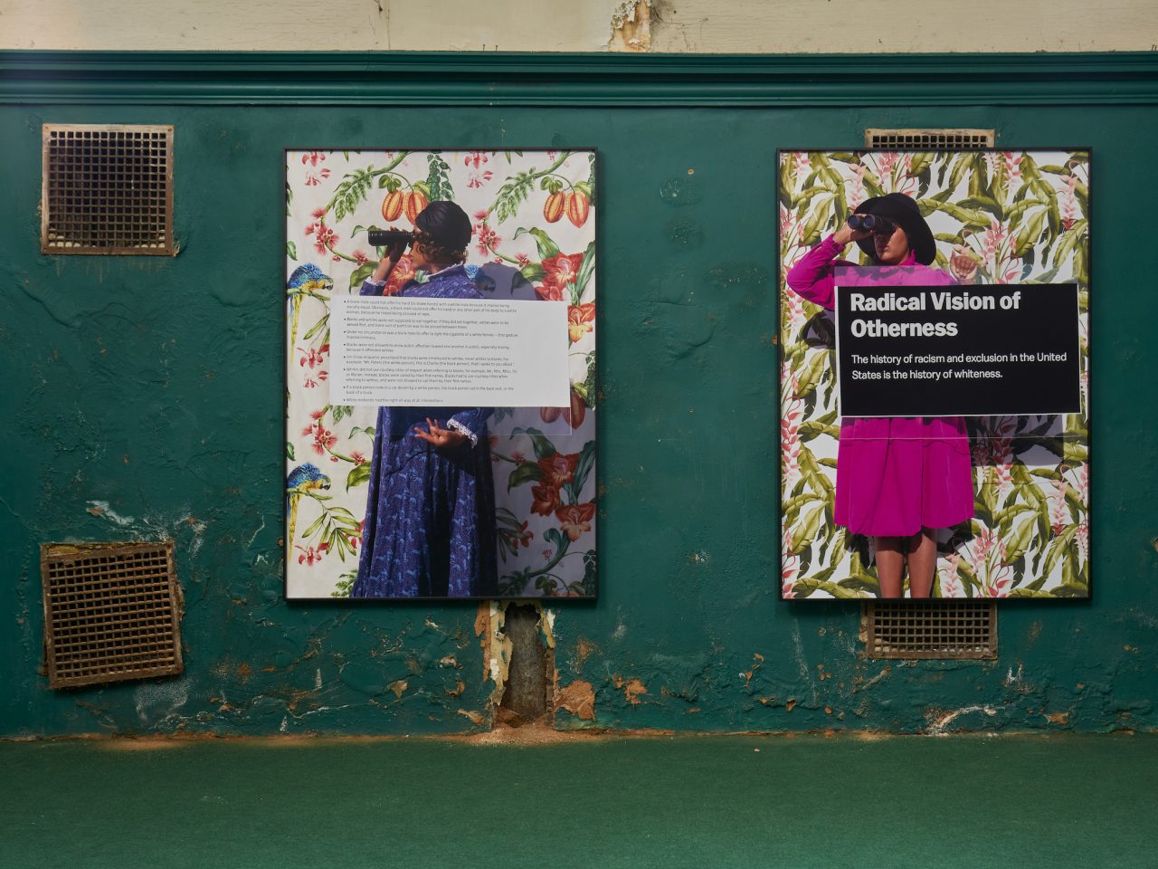 Two large flat artworks on the walls of Cotton Exchange, the artworks have flowery assets to them, both with women looking through binoculars and blacks of text infront of them. The text eligible reads 'Radical Vision of Otherness'. The space had dark green walls and a green carpet.