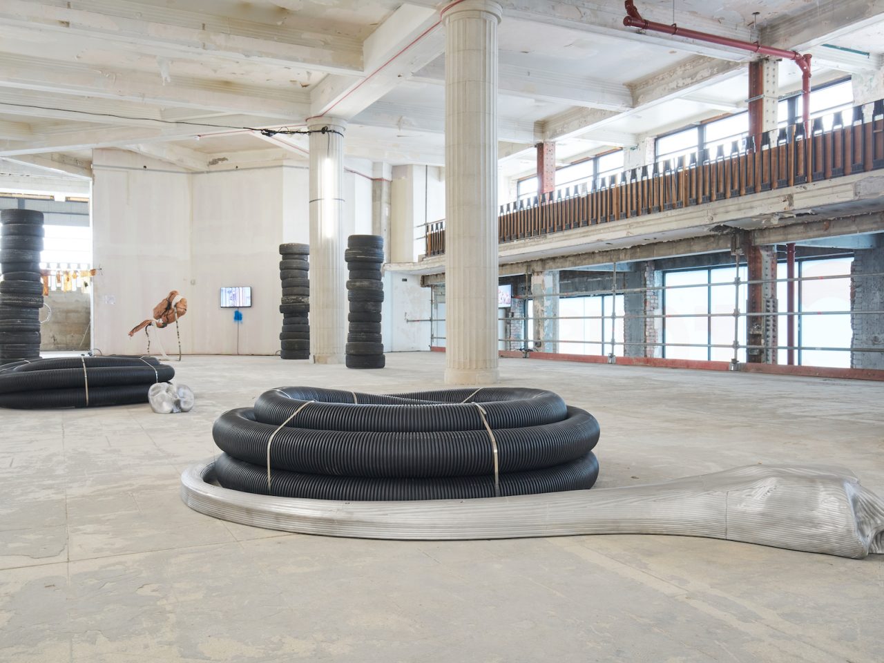 Large floor sculptures, they are long black tubes tied together to create a circular structure, underneath them is a large-scale stretched aluminium model of a human bone curving outwards.
