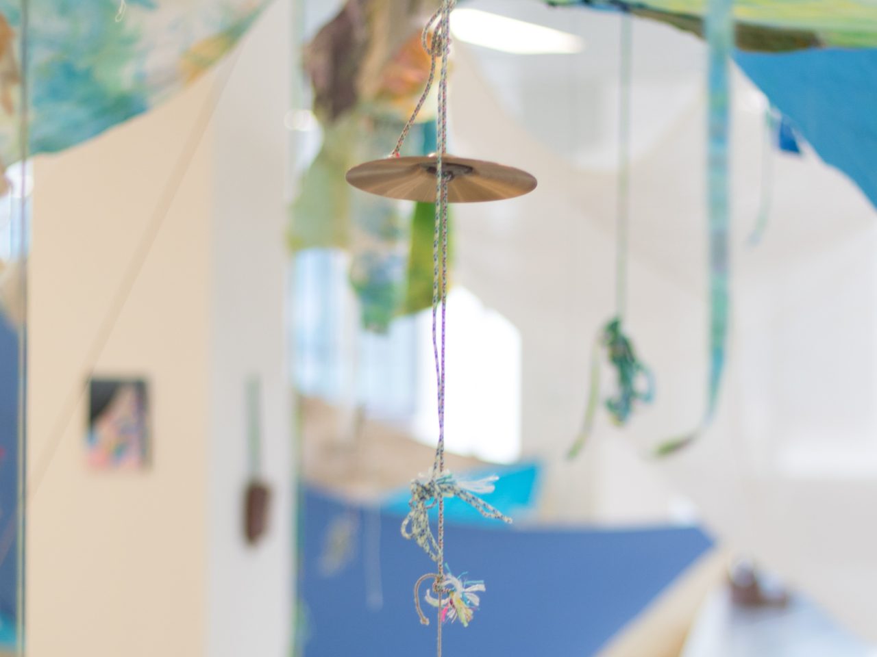 A detail shot of a small percussion cymbal hung on a colourful piece of string.