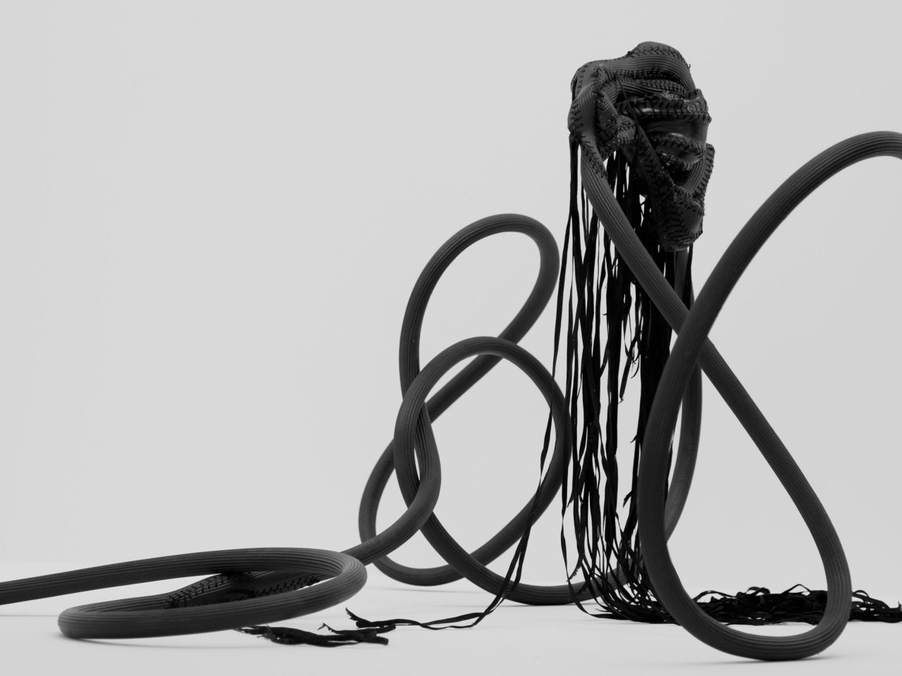 A close up of a sculpture that shows a black tangled hosepipe thanding up with drapped ribbons from its highest point.