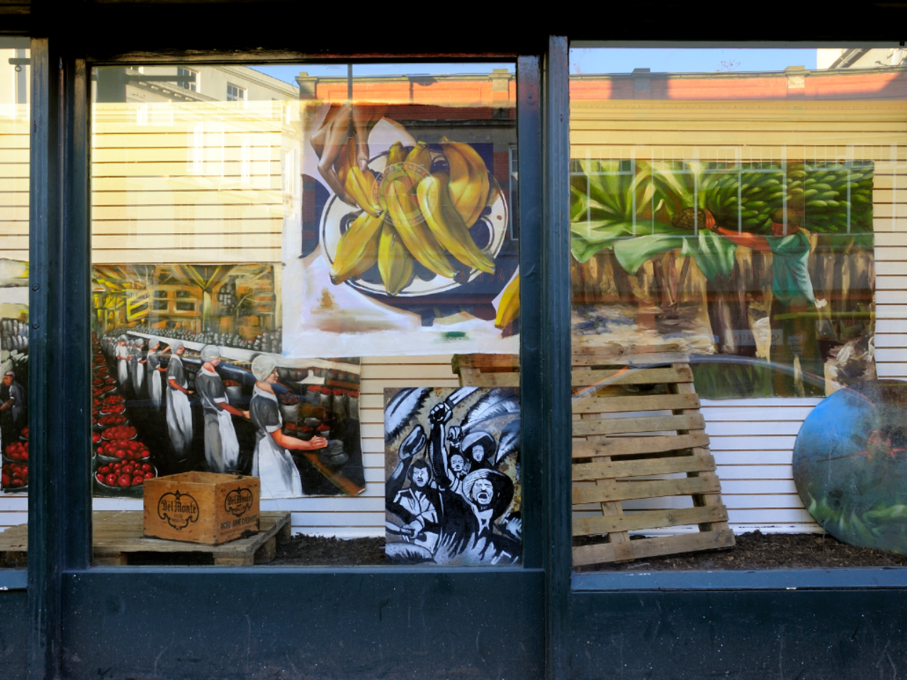 A window display. in the window display is various paintings, large and small, rectangular and circular, there's also wooden pallets in the space.
