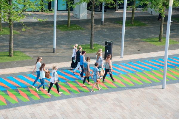 A group of 11 people walking along a blue, green and orange pathway in the city.