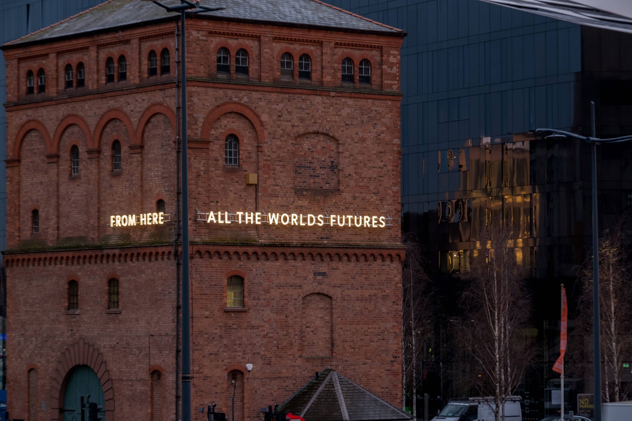 A close up of a building, the building has glowing lights reading 'from here, all the worlds futures'