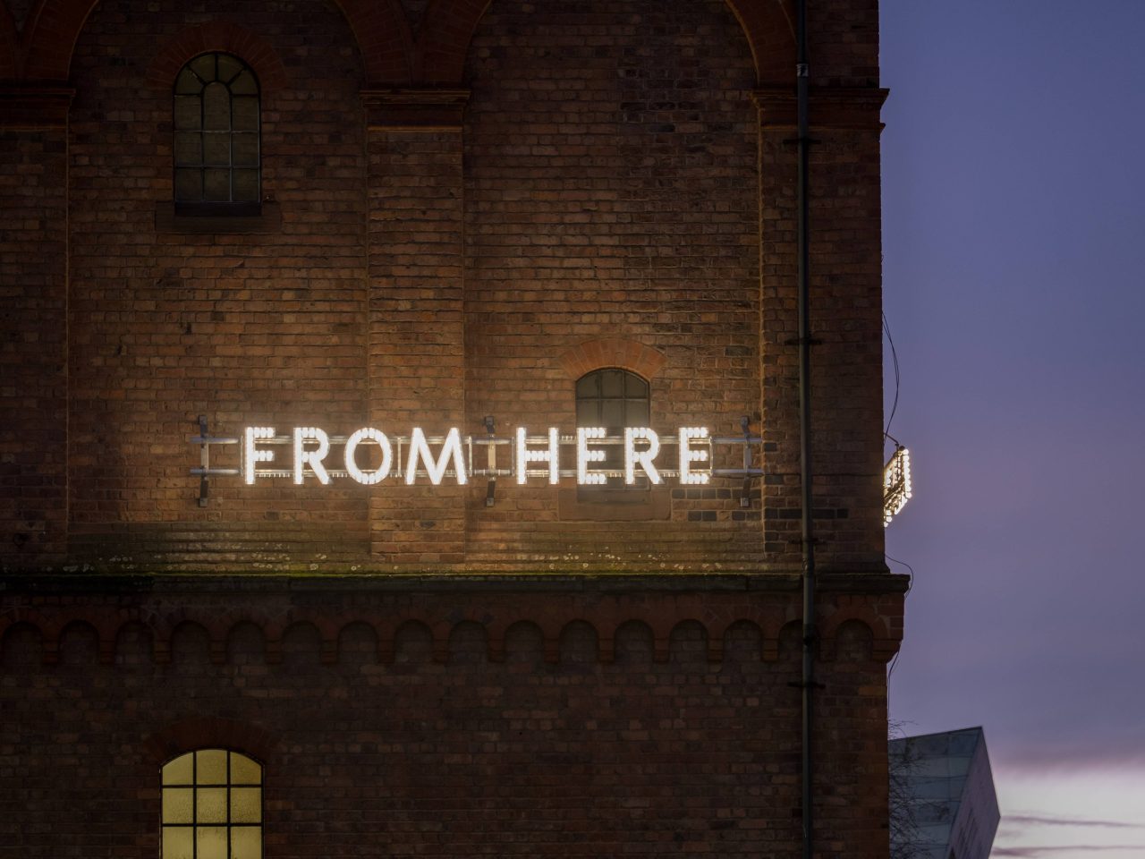 A close up of a building, the building has glowing lights reading 'From Here'