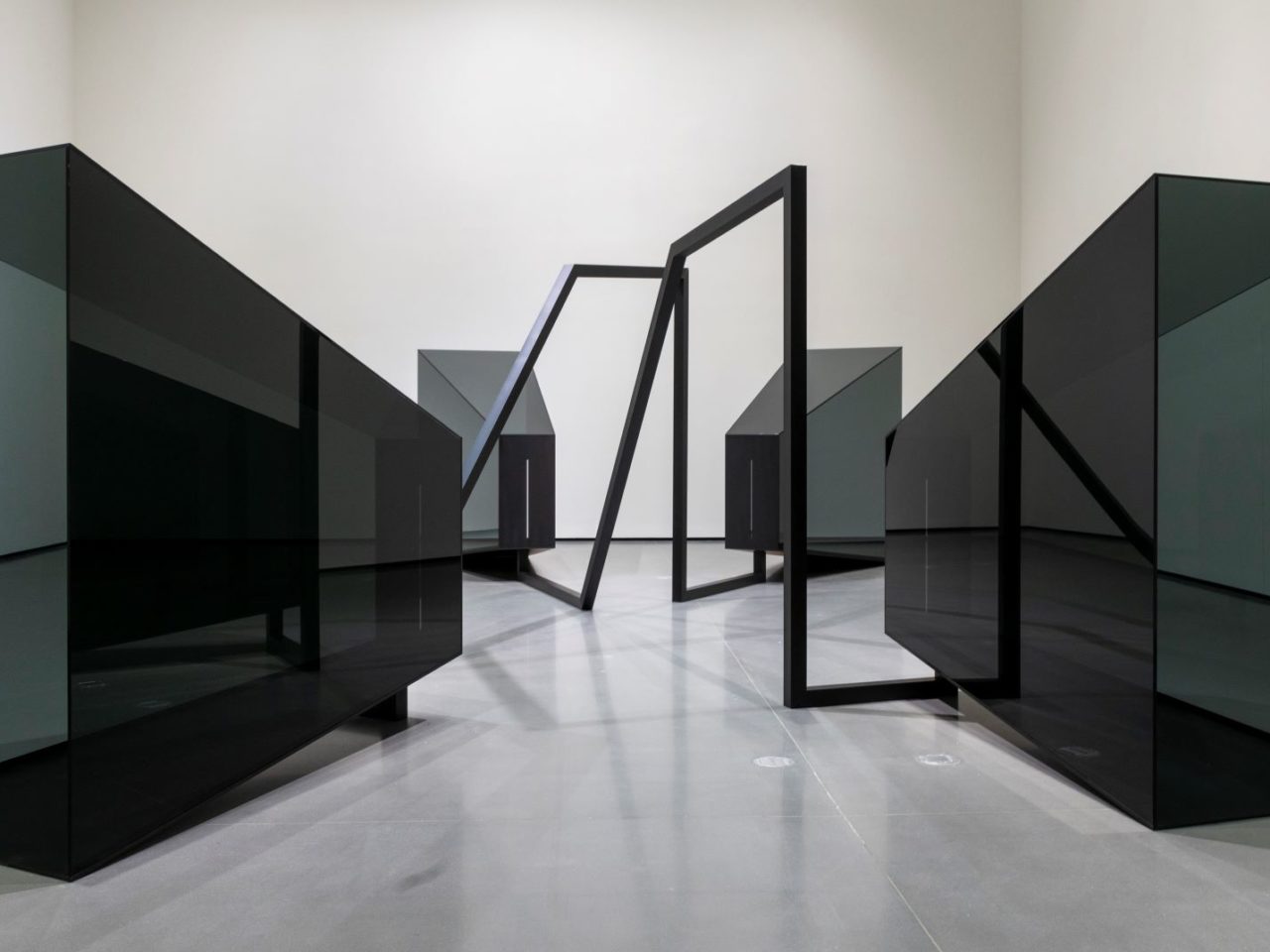 An installation in a white room, the installation is four large reflective black cuboids pointing towards each other with connecting tails