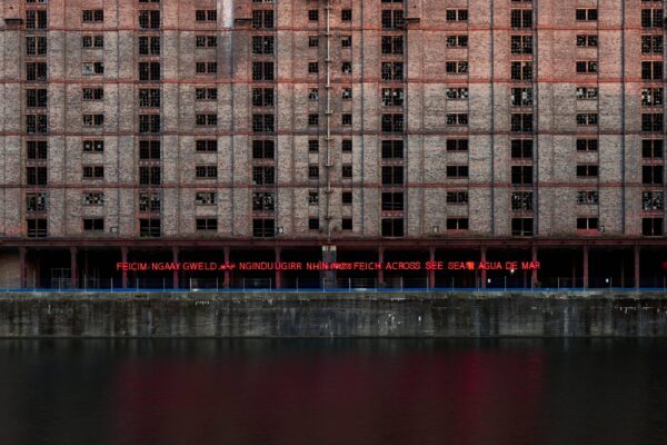 a red neon artwork on Stanley Dock, the sign is attached to Tobacco Warehouse, the sign reads 'to see' in several different languages.⁠