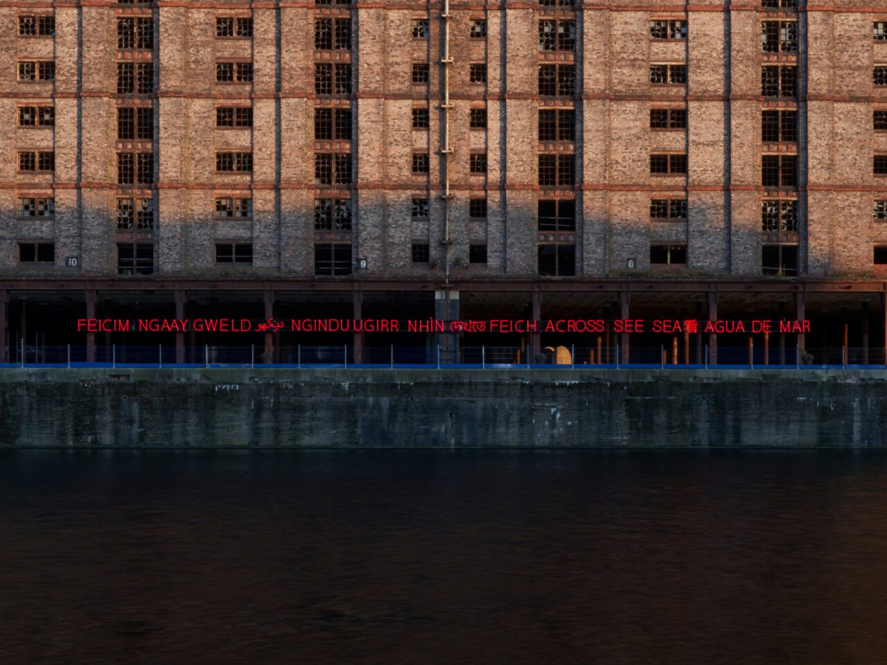 a red neon artwork on Stanley Dock, the sign is attached to Tobacco Warehouse, the sign reads 'to see' in several different languages.⁠