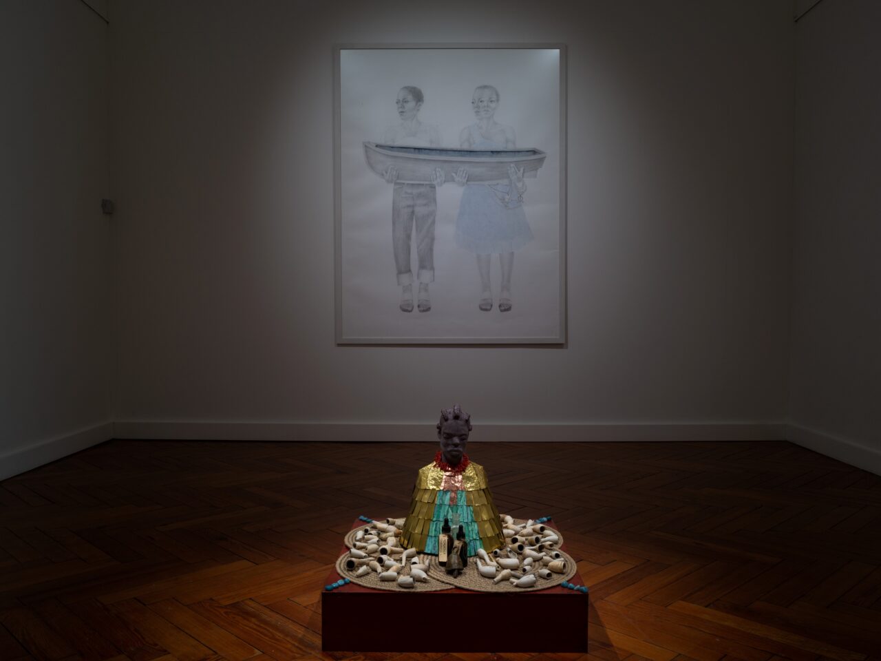 an installation with large pencil drawings on the walls and in the centre of the room is a shrine made up of found objects and a sculpture of the artist