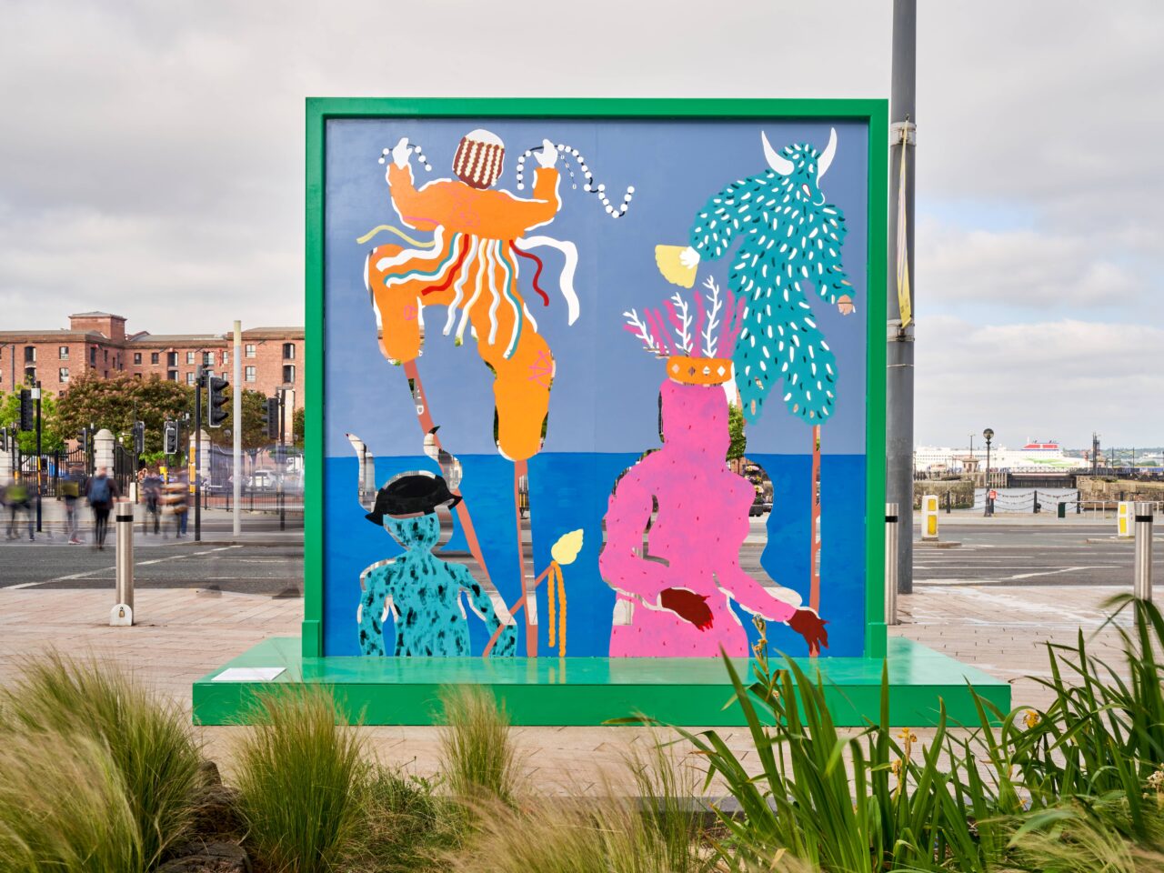 A colourful sculpture made of hand painted sheet metal. Parts of the metal has been cut out, so that it casts shadows onto the street.