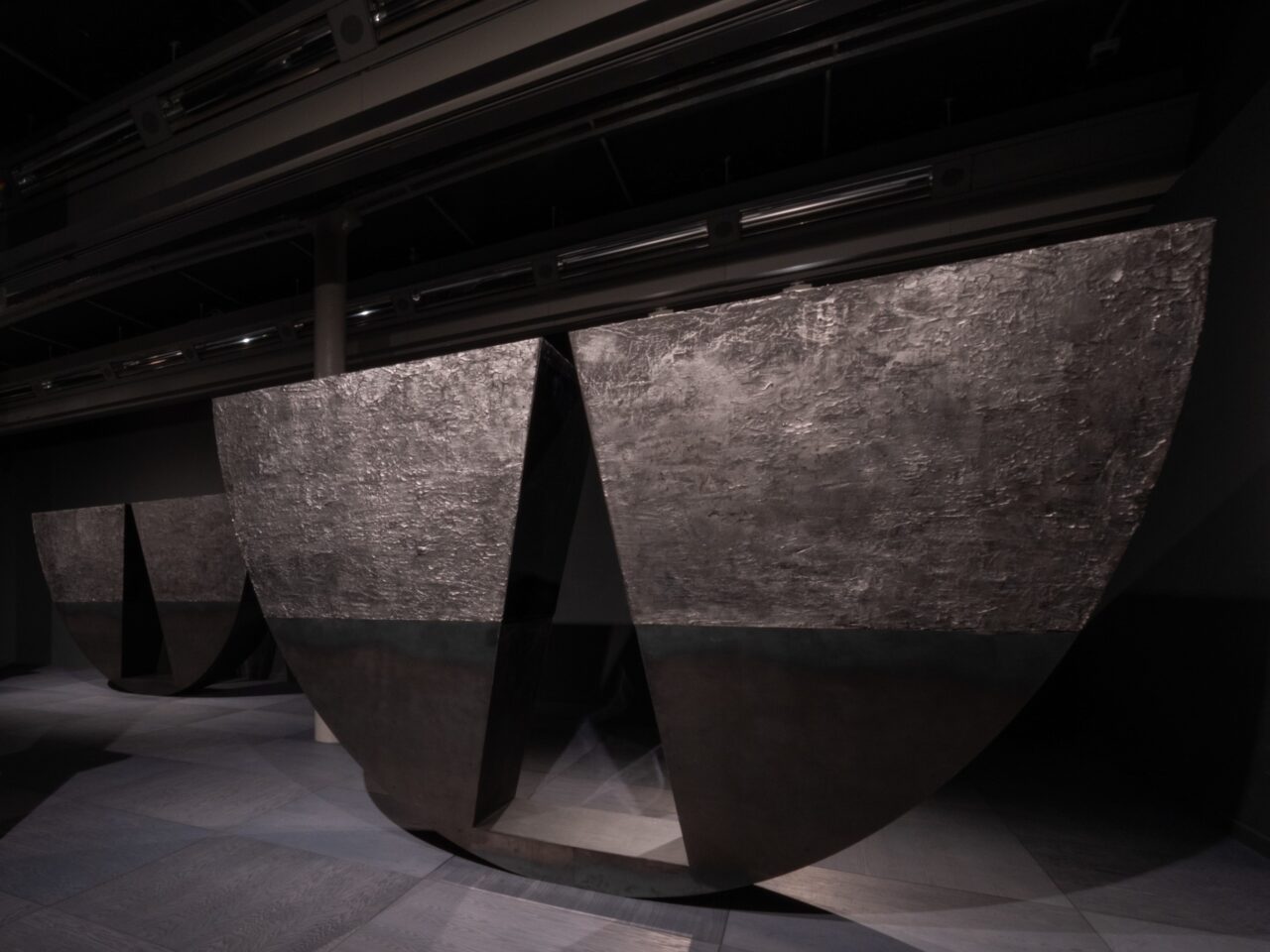 Monumental, curved, grey sculptures in a dark gallery space