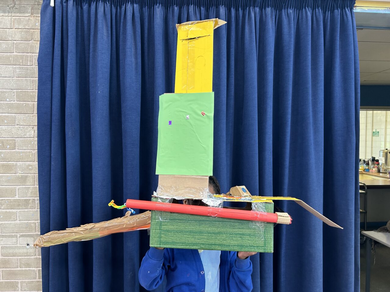 A tall cardboard built machine with tin foil, tubes and coloured paper.