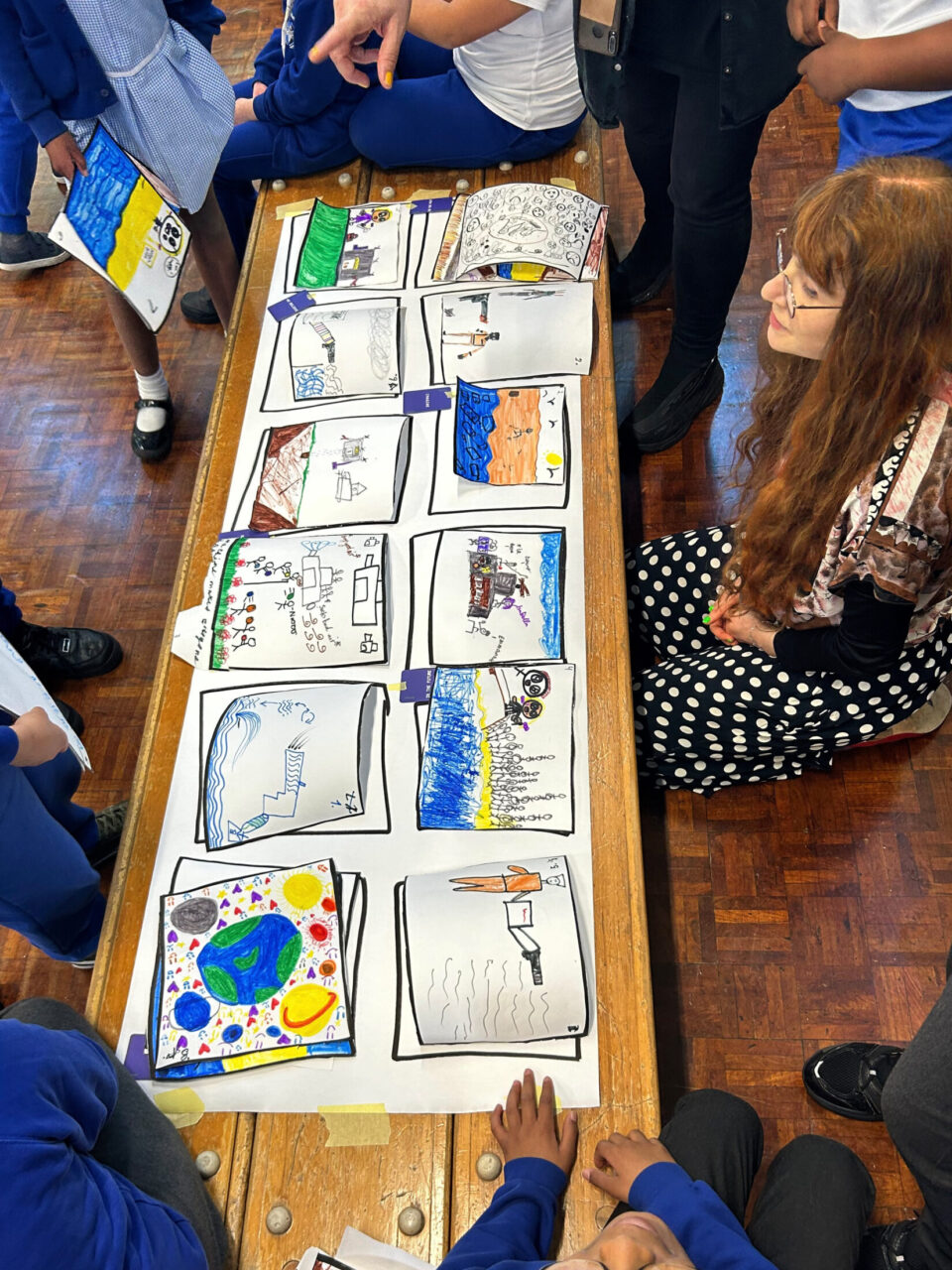 A group of children working with Stine and Aleks to create a story board out of their drawings.